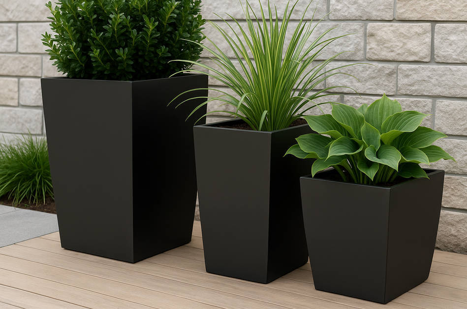 Group of matte black planters filled with lush green plants arranged on a light stone patio, creating contrast against wooden decking in a modern outdoor space.